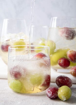Four glasses filled with non-alcoholic spritzer and frozen grapes.