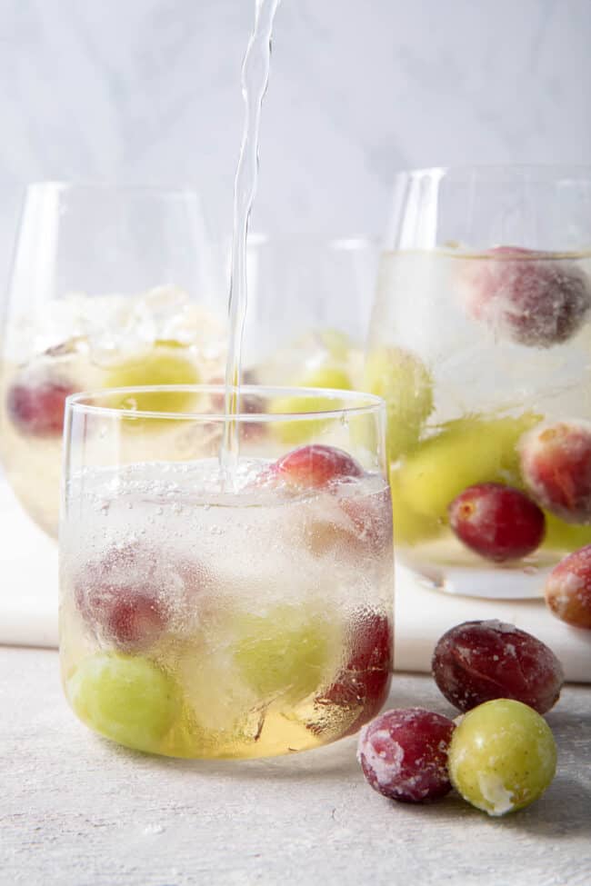 clear drinking glasses filled with white grape spritzer and frozen grapes