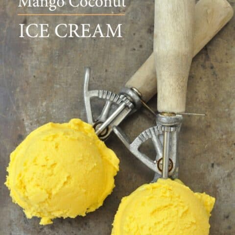 Two ice cream scoops with wooden handles have scoops of mango ice cream in them.