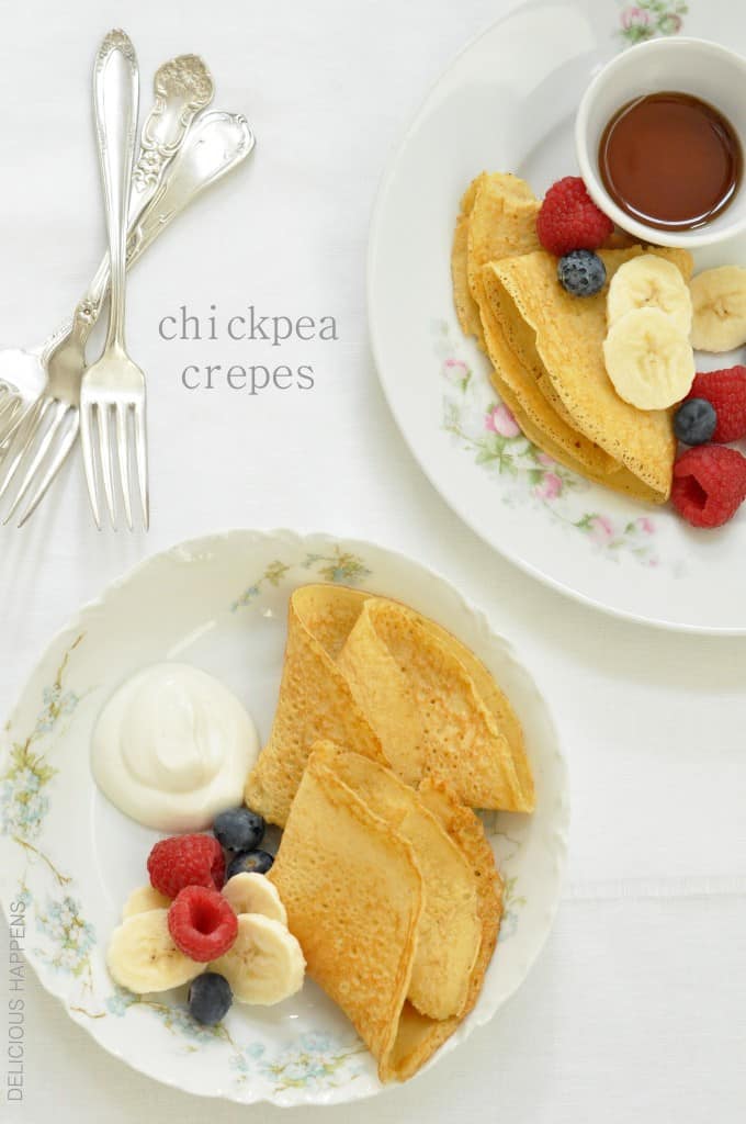 Two white plates with chickpea crepes, fresh fruit and a small white bowl of pure maple syrup.