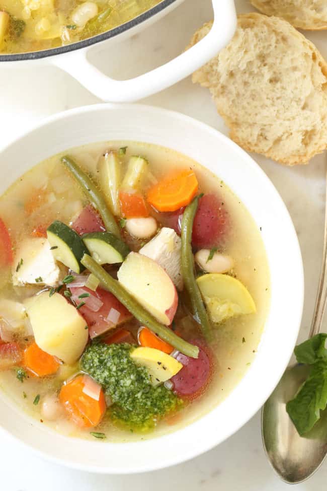 A white bowl filled with Soupe au Pistou (French chicken vegetable soup). A spoon rests near the bowl.