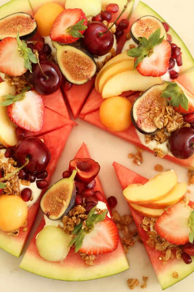 Slices of watermelon with slices of fruit and granola on each slice.