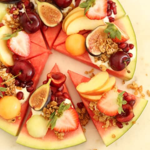 Slices of watermelon pizza with yogurt and slices of fruit on top of each slice.