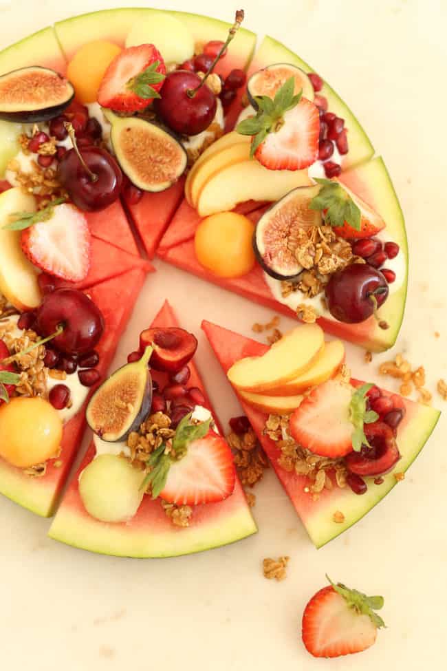 Slices of watermelon with yogurt and slices of fruit on top of each slice.