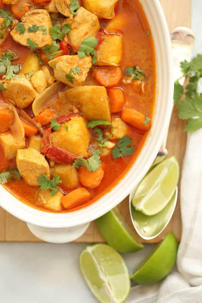 A white bowl filled with Thai coconut curry chicken. Lemon wedges sit next to the bowl.