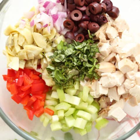 A clear glass mixing bowl filled with Italian Chicken Salad ingredients.