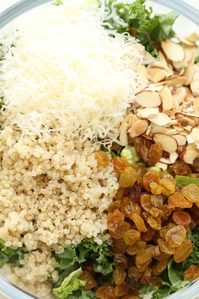 A clear glass bowl of curly kale salad with quinoa and raisins.