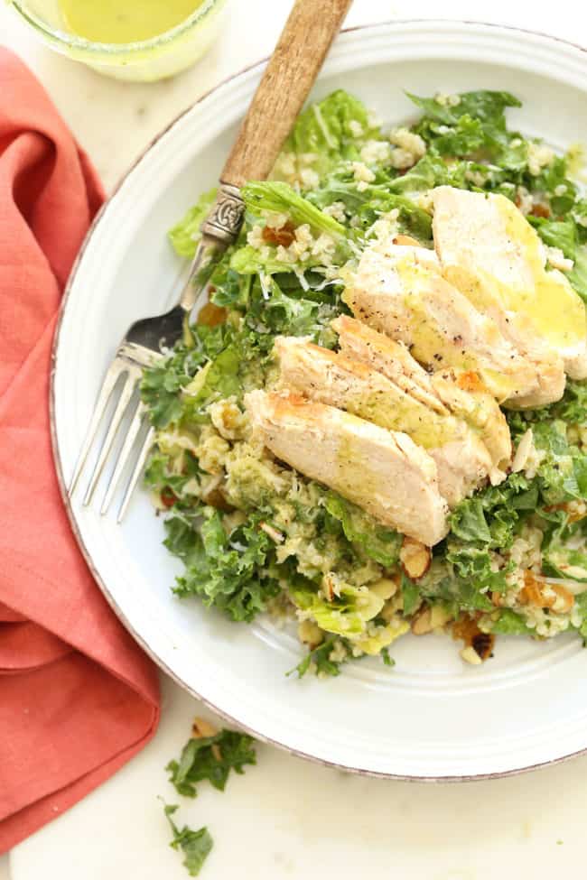 A white plate of curly kale salad with quinoa and grilled chicken.