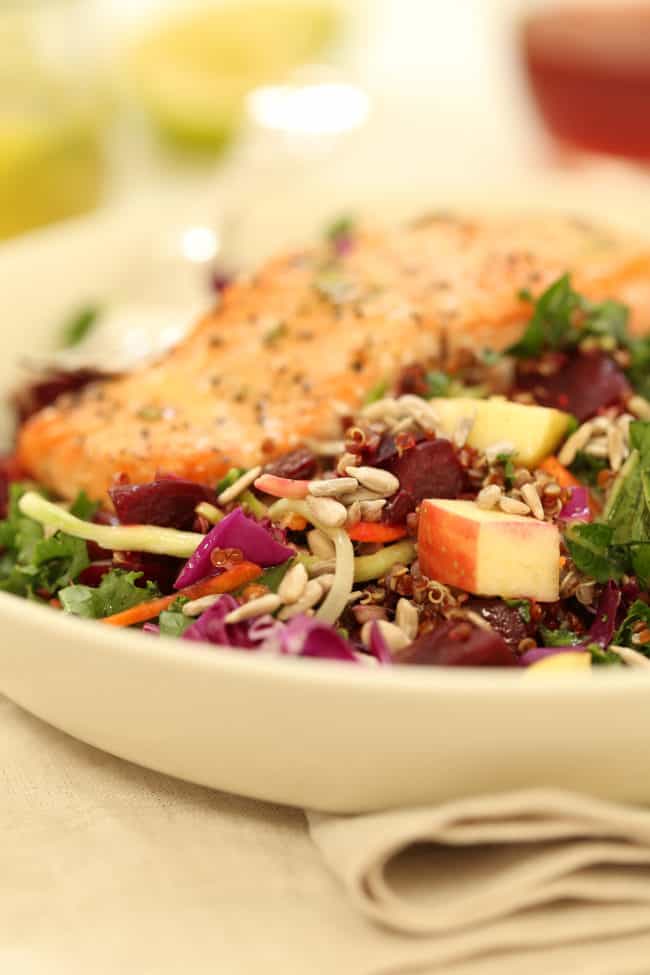 A white bowl of tossed greens with salmon fillet. 