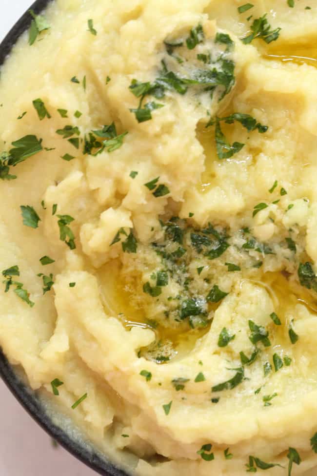 A dark brown bowl filled with Mashed Sweet Potatoes topped with roasted garlic parsley butter.