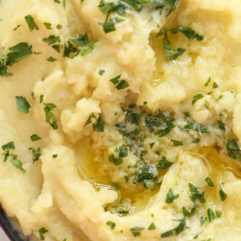 A dark brown bowl filled with Mashed Sweet Potatoes with Roasted Garlic Parsley Butter.