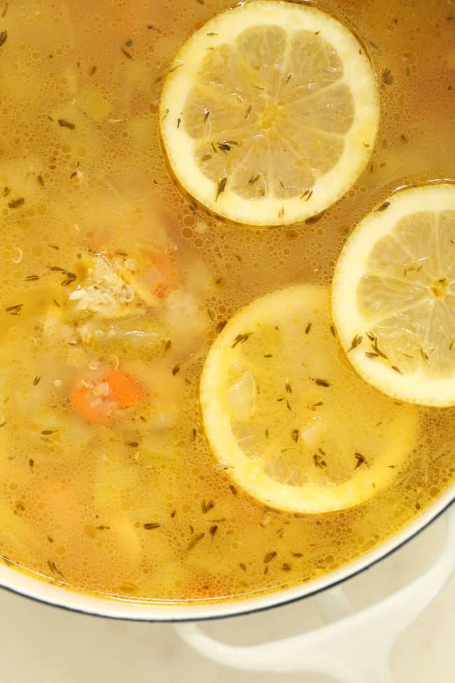 A white pot filled with broth. Citrus slices float in the broth.