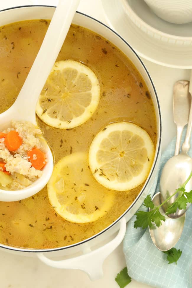 a white pot filled with lemon chicken quinoa soup. A white ladle rests in the pot.