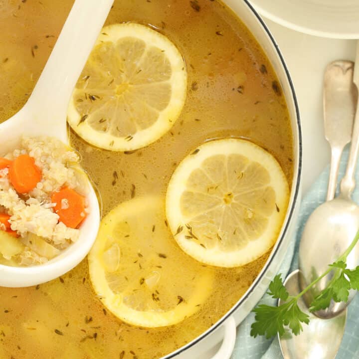 A white pot filled with Lemon Chicken Quinoa Soup. A white ladle rests in the pot.