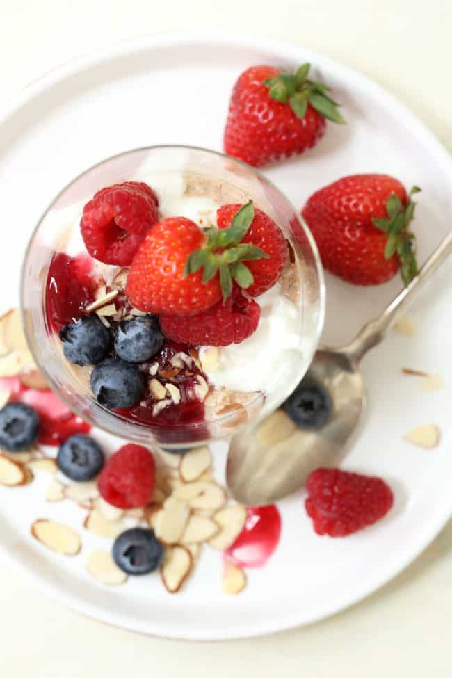 A clear glass filled with breakfast cereal, yogurt and fruit.