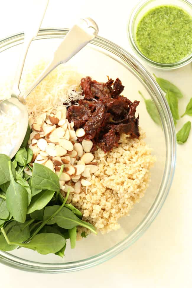 A clear bowl of spinach and quinoa salad ingredients.
