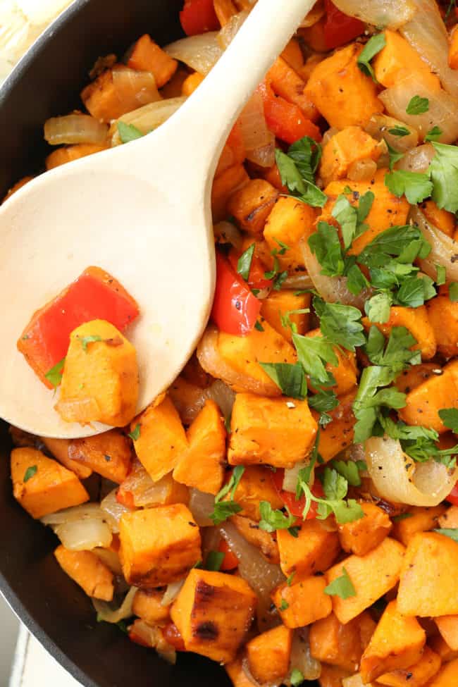 A black skillet filled with sweet potatoes, onions and red bell pepper.