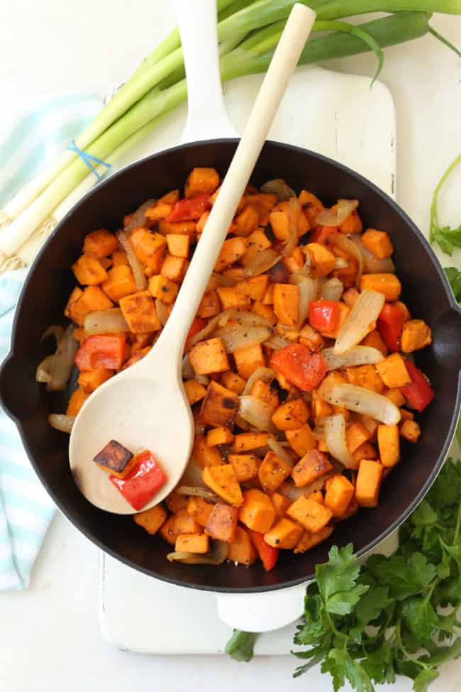 A white skillet filled with pan roasted sweet potatoes with onion and red pepper.