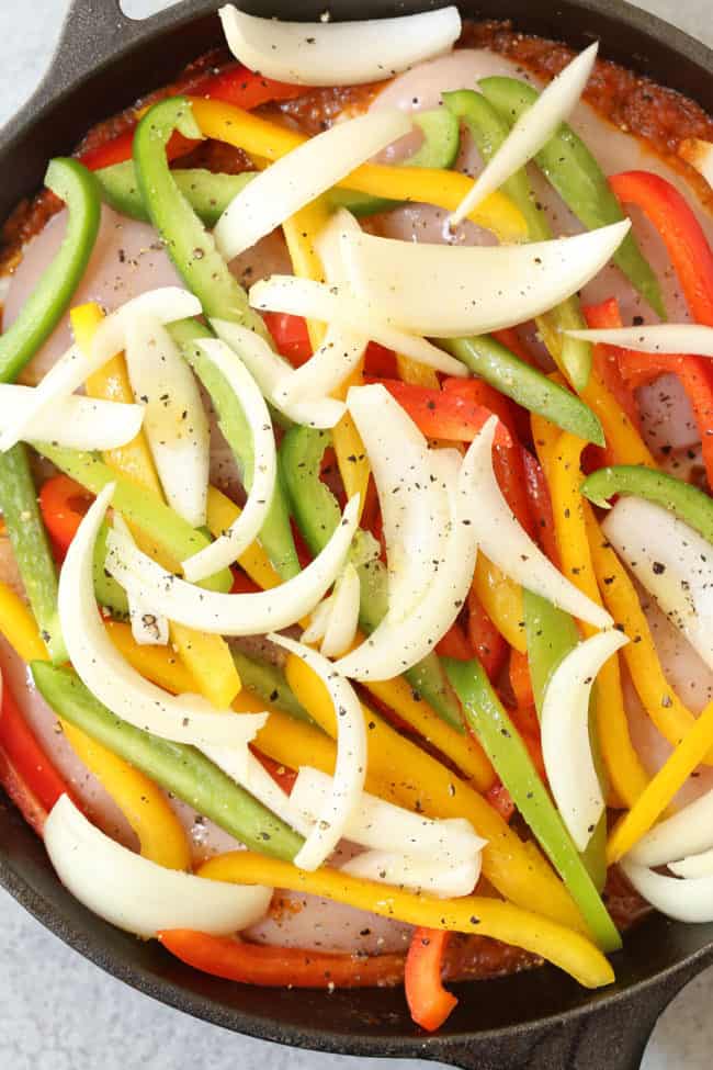 A black cast iron skillet filled with onions and peppers.