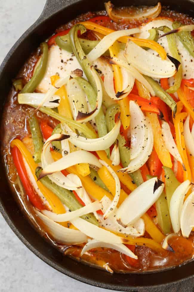 A black cast iron skillet filled with onions and peppers for a baked chicken fajita recipe.