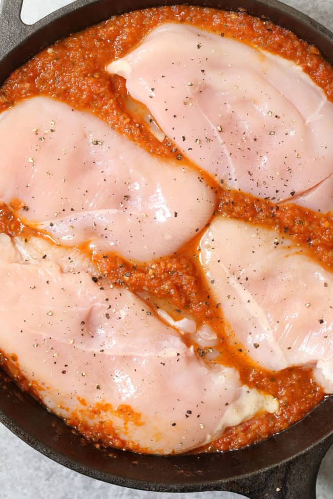 A cast iron skillet filled with raw poultry tucked in a red sauce.