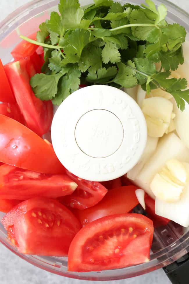 A food processor filled with tomatoes, onion, garlic and cilantro.