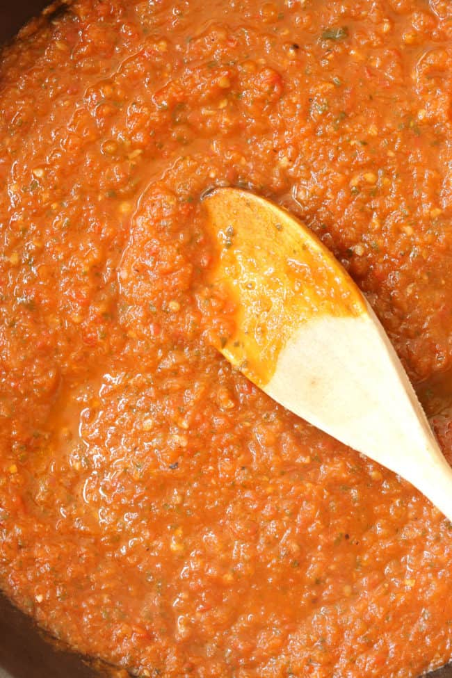 A black skillet filled with a Mexican red sauce. A wooden spoon rests in the skillet.