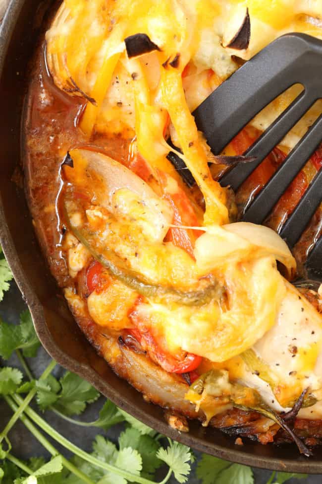 A black skillet filled with Easy Chicken Fajita Bake. A spatula rests in the skillet.