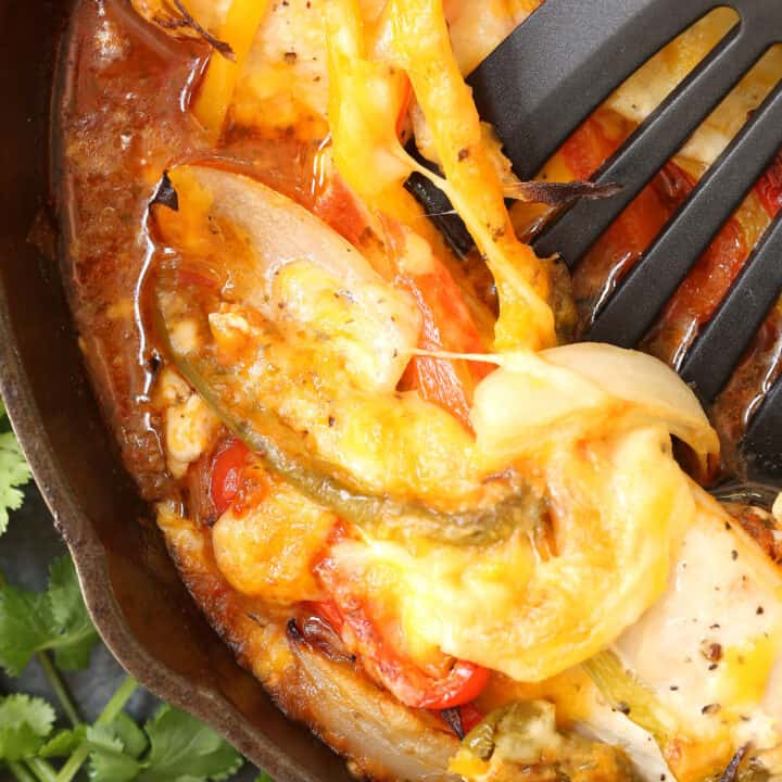 A cast iron skillet filled with chicken fajita bake. A spatula rests in the skillet.