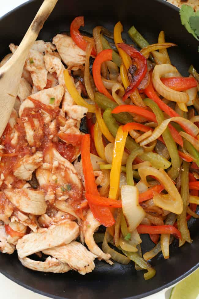 A black cast iron skillet filled with cooked poultry strips and grilled vegetables for recipe for baked quesadillas.