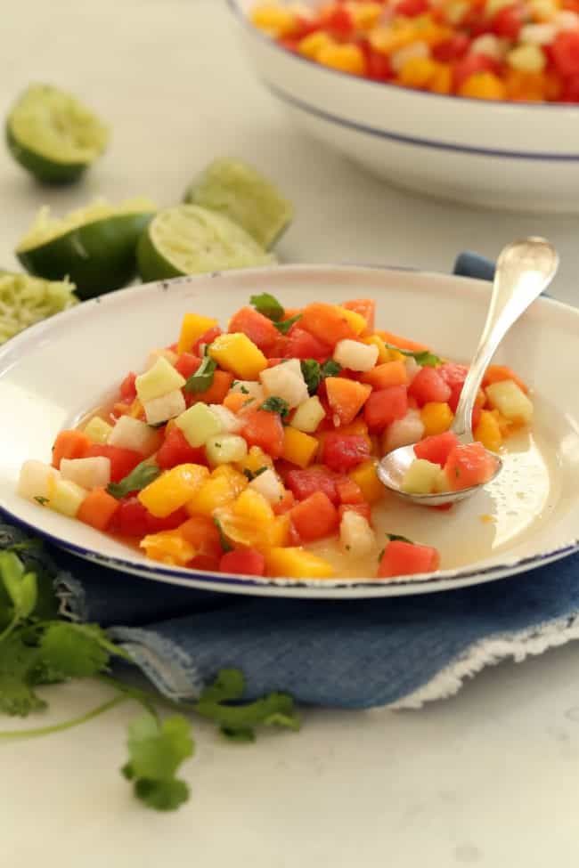 A white plate of chopped fruit salad with a spoon.