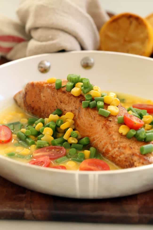 A white skillet with a piece of cooked fish smothered in chopped green beans and corn.