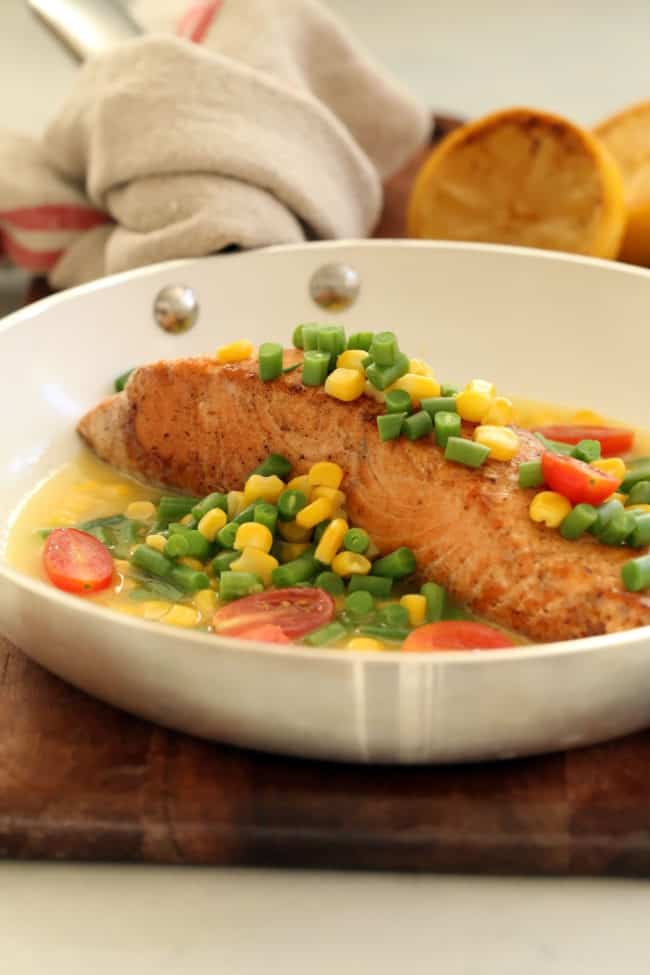 A white skilled with a piece of pan seared salmon smothered in chopped green beans and corn.