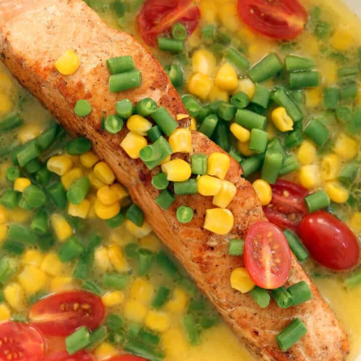 A white skillet with pan seared salmon smothered in chopped green beans and corn.