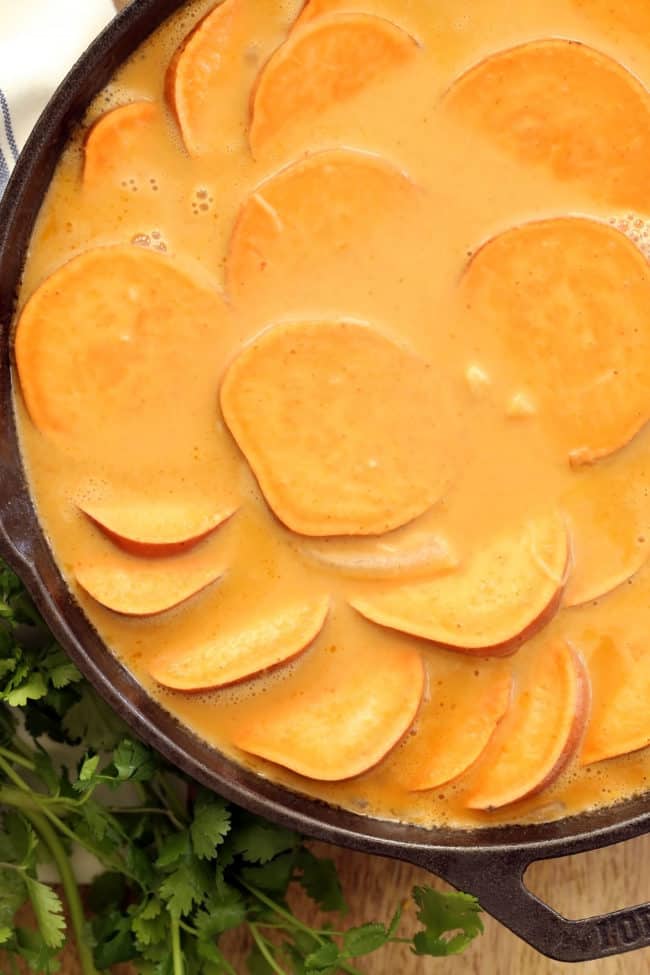 A black cast iron skillet filled with coconut curry scalloped sweet potatoes.