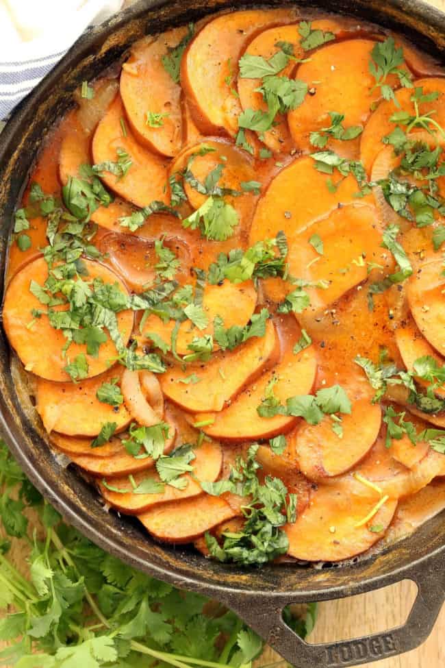 A black cast iron skillet filled with coconut curry scalloped sweet potatoes.