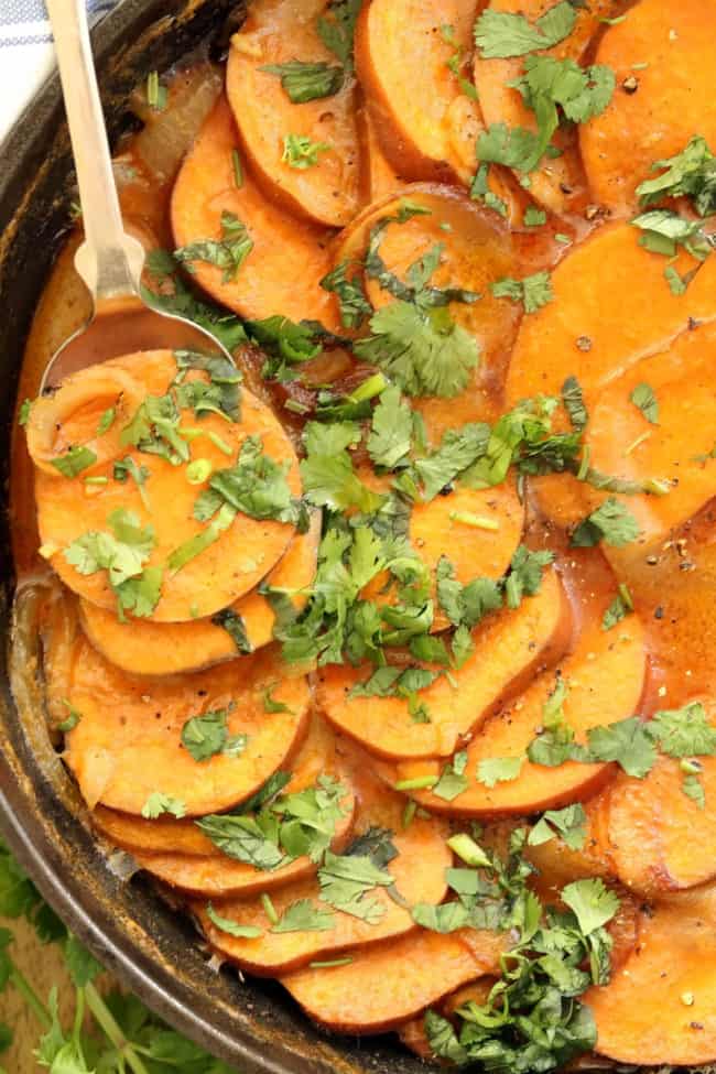 A black cast iron skillet filled with scalloped sweet potatoes.