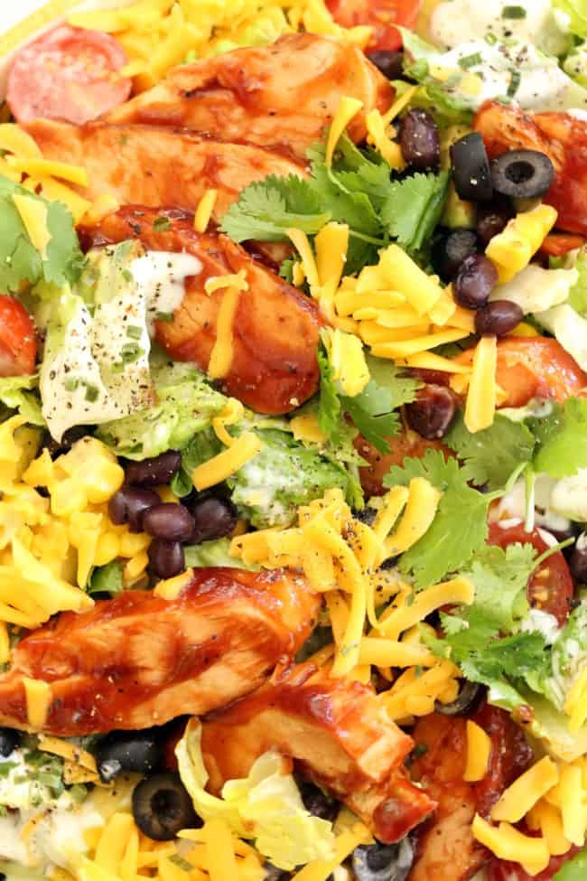 A bowl filled with lettuce, black beans, corn, avocado and grated cheddar cheese 