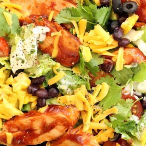 A bowl filled with lettuce, black beans, corn, avocado, grated cheddar cheese and BBQ chicken tossed in ranch dressing