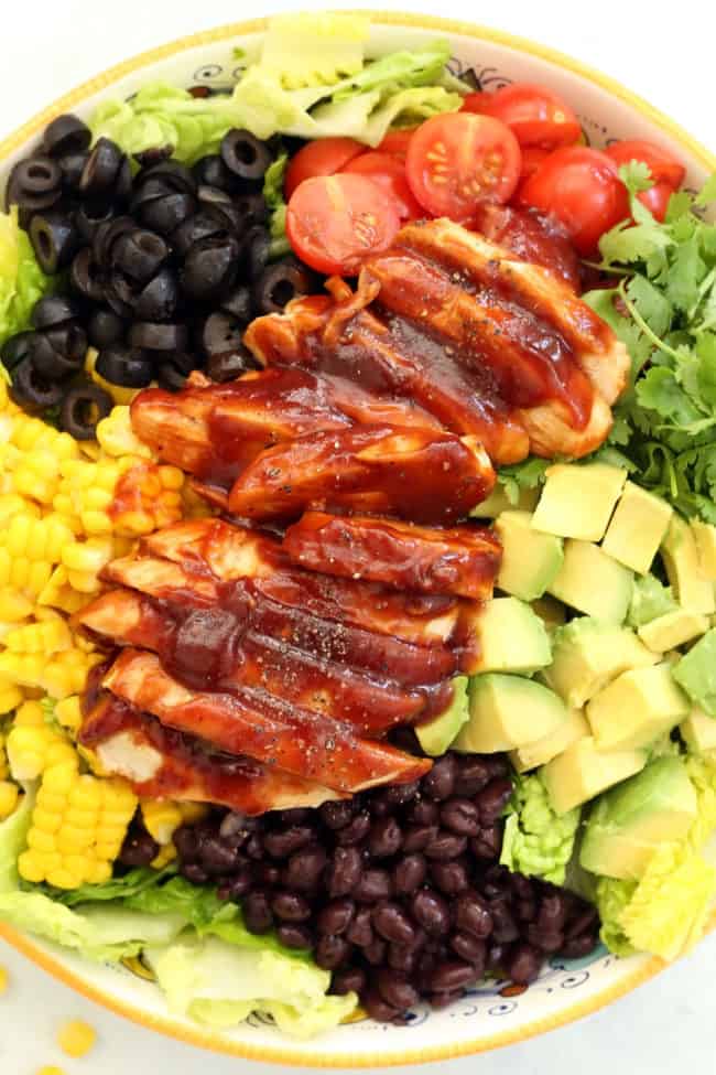 A bowl filled with lettuce, black beans, corn, avocado and BBQ chicken