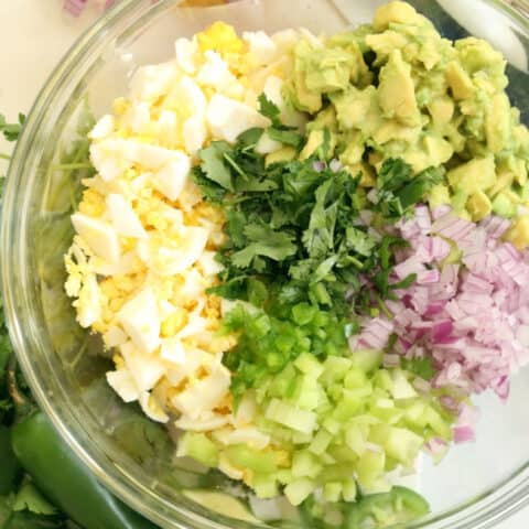 A clear glass bowl of mashed hard boiled egg and avocado.