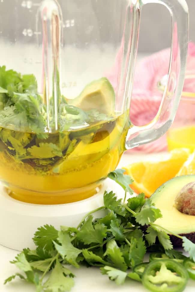 A clear glass blender filled with olive oil, orange juice and cilantro. 