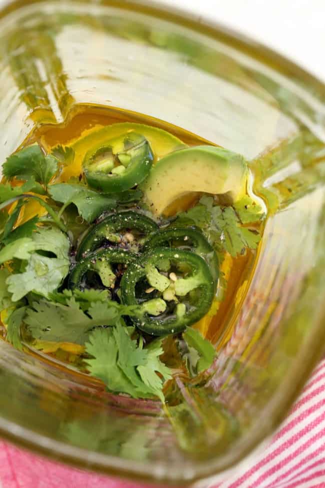 A clear glass blender filled with avocado dressing ingredients - avocado, cilantro, jalapeno and olive oil.