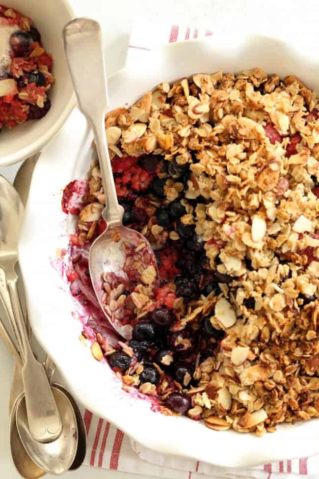 A white pie dish filled with mixed berry crisp. A silver spoon rests in the dish.