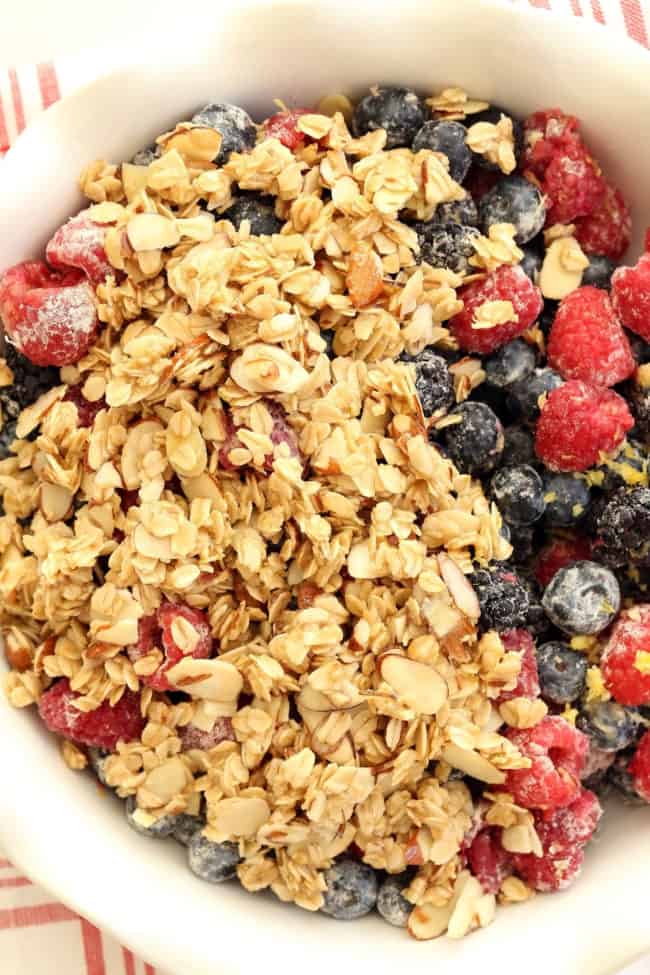 A white pie dish filled with fruit and crumb topping made with oats and sliced almonds