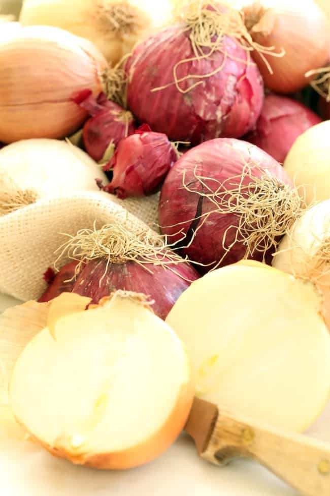 Several red, brown and white onions are scattered on a counter with a knife sitting next to them.