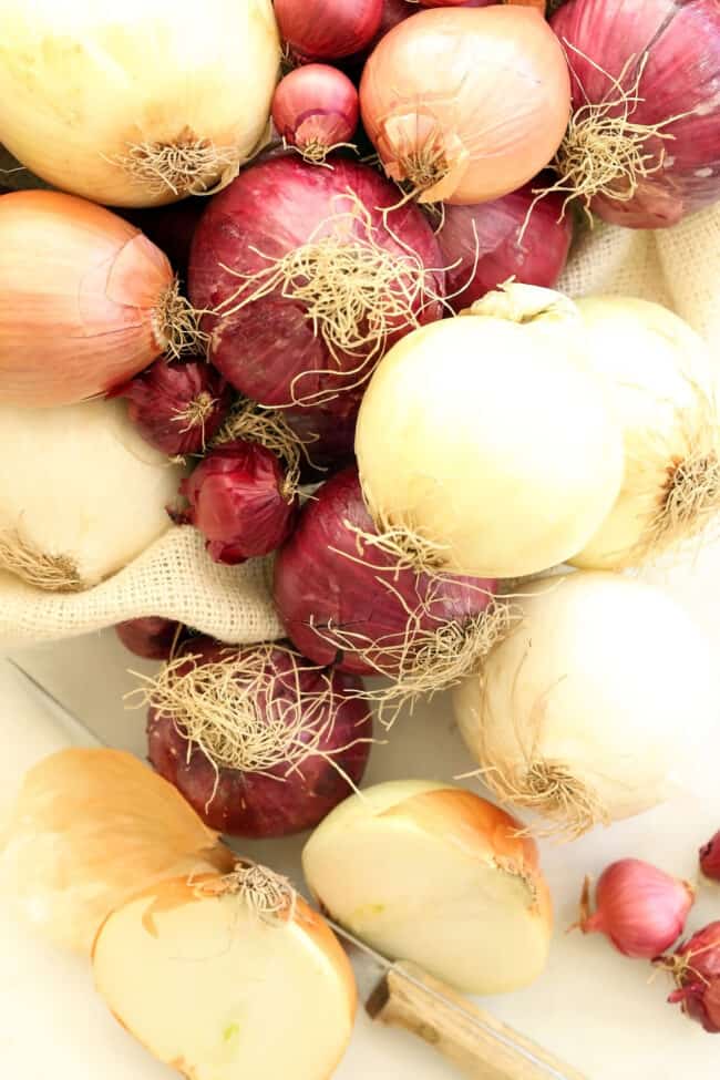 Several red, brown and white onions are scattered on a counter with a knife sitting next to them.