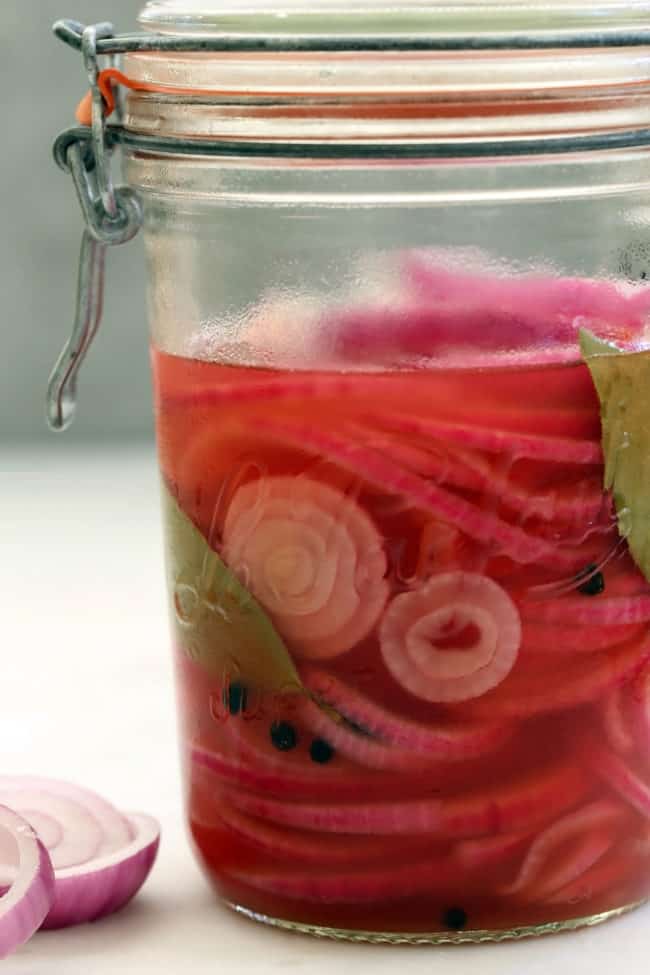 A clear glass mason jar filled with pickled red onions.