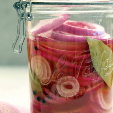 A clear glass mason jar filled with pickled red onions.