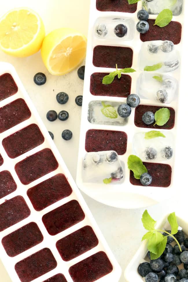 Two white ice cube trays filled with blueberry ice cubes.